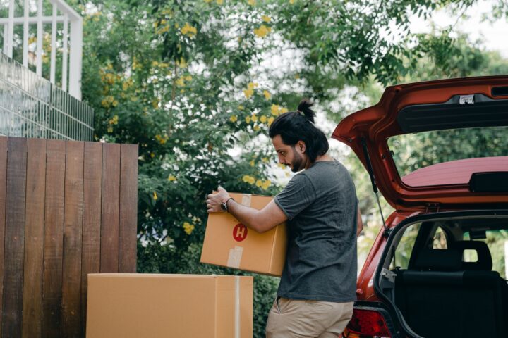 young-male-taking-boxes-out-of-luggage-boot-of-car